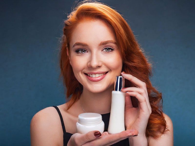 Smiling woman holding two skincare product containers against a blue background.